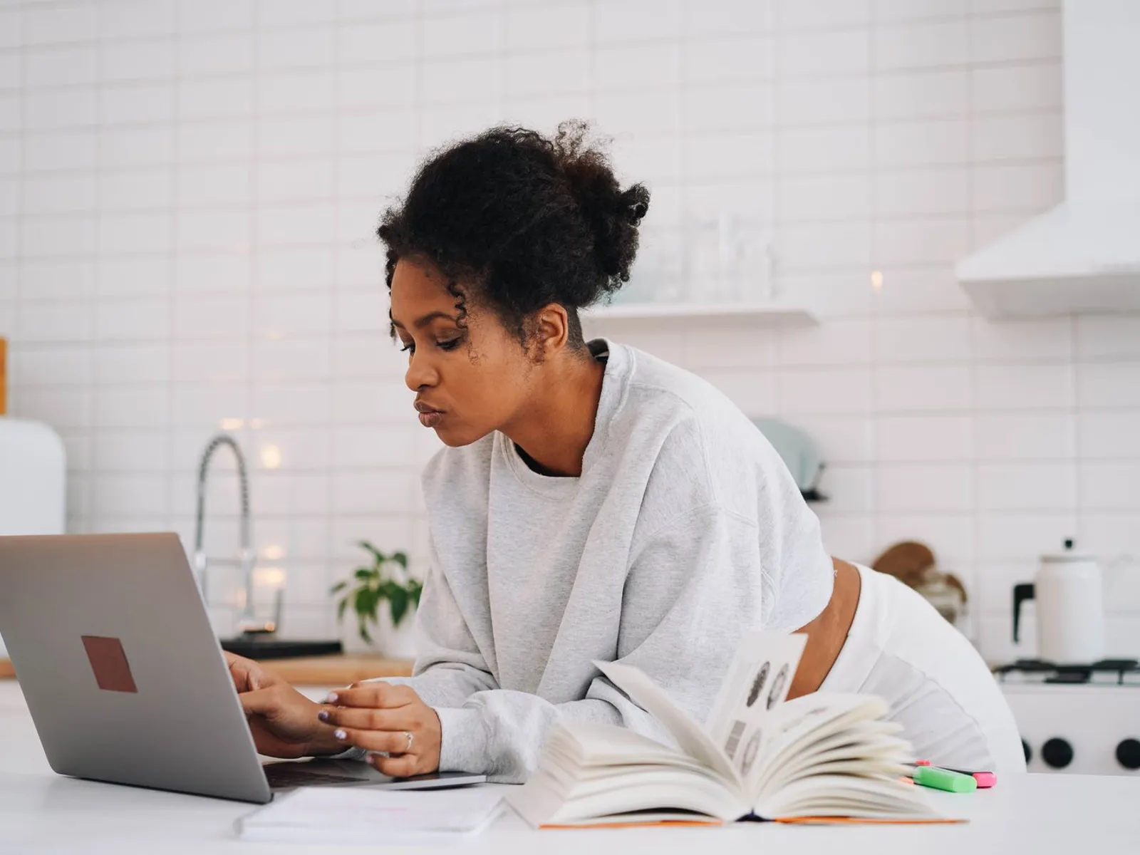 A learner studying at a kitchen table with a laptop and notes